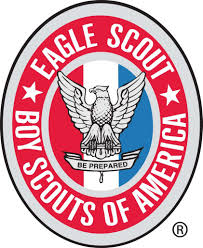Oval emblem with the words "Eagle Scout Boy Scouts of America" surrounding a gray eagle perched on a red, white, and blue background. The eagle holds a ribbon with the phrase "Be Prepared.