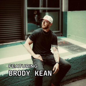 A man in a black t-shirt and light cap sits on a green concrete ledge outdoors. Text on the image reads: "FEATURING BRODY KEAN." The background shows an urban setting with windows and a garage door.