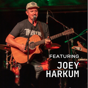 A man wearing a cap and T-shirt plays an acoustic guitar and sings into a microphone on stage. Text reads "Featuring Joey Harkum." Drums and stage lights are visible in the background.